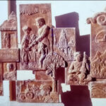 Terracotta-colored fiberglass bas-relief wall mural. The collage depicts several square and rectangular panels illustrating scenes of everyday rural life, including religious symbols, farming, and heritage.